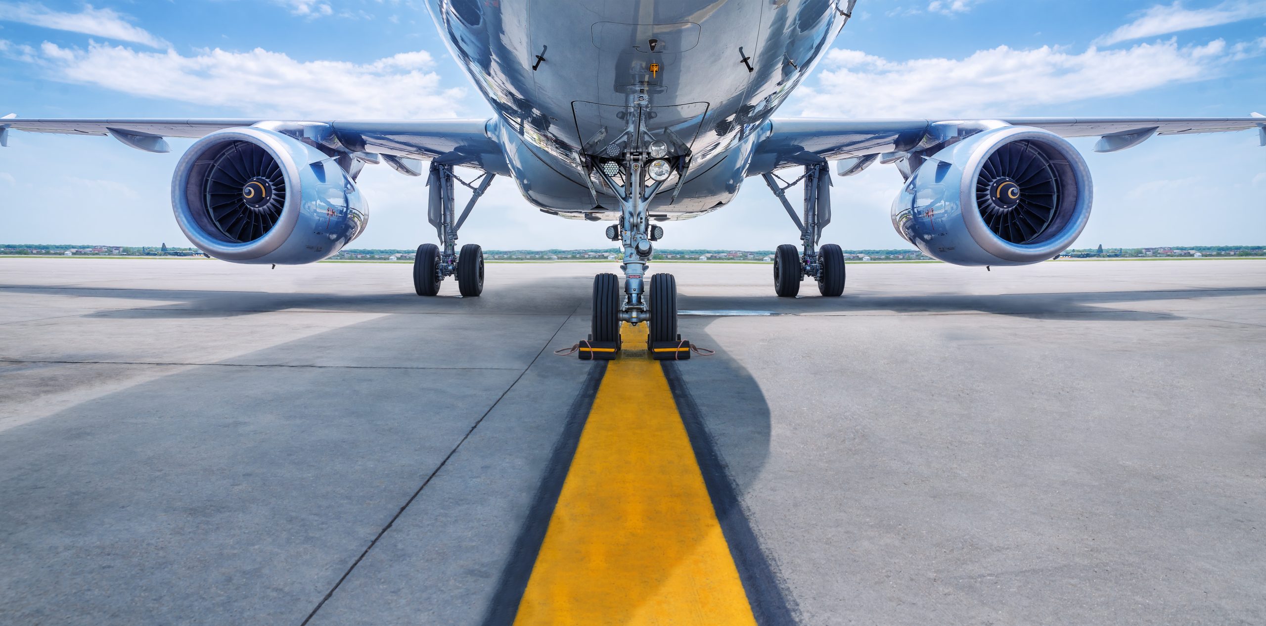The underside view of an airplane with a yellow line on the ground