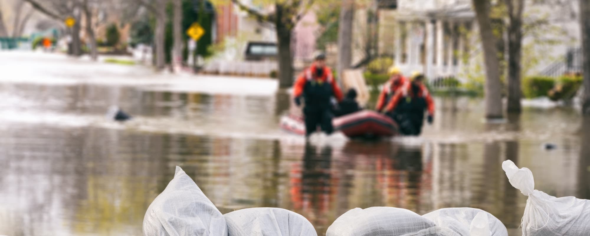 Flooded street with sandbags in the foreground and a rescue team in a boat in the background.