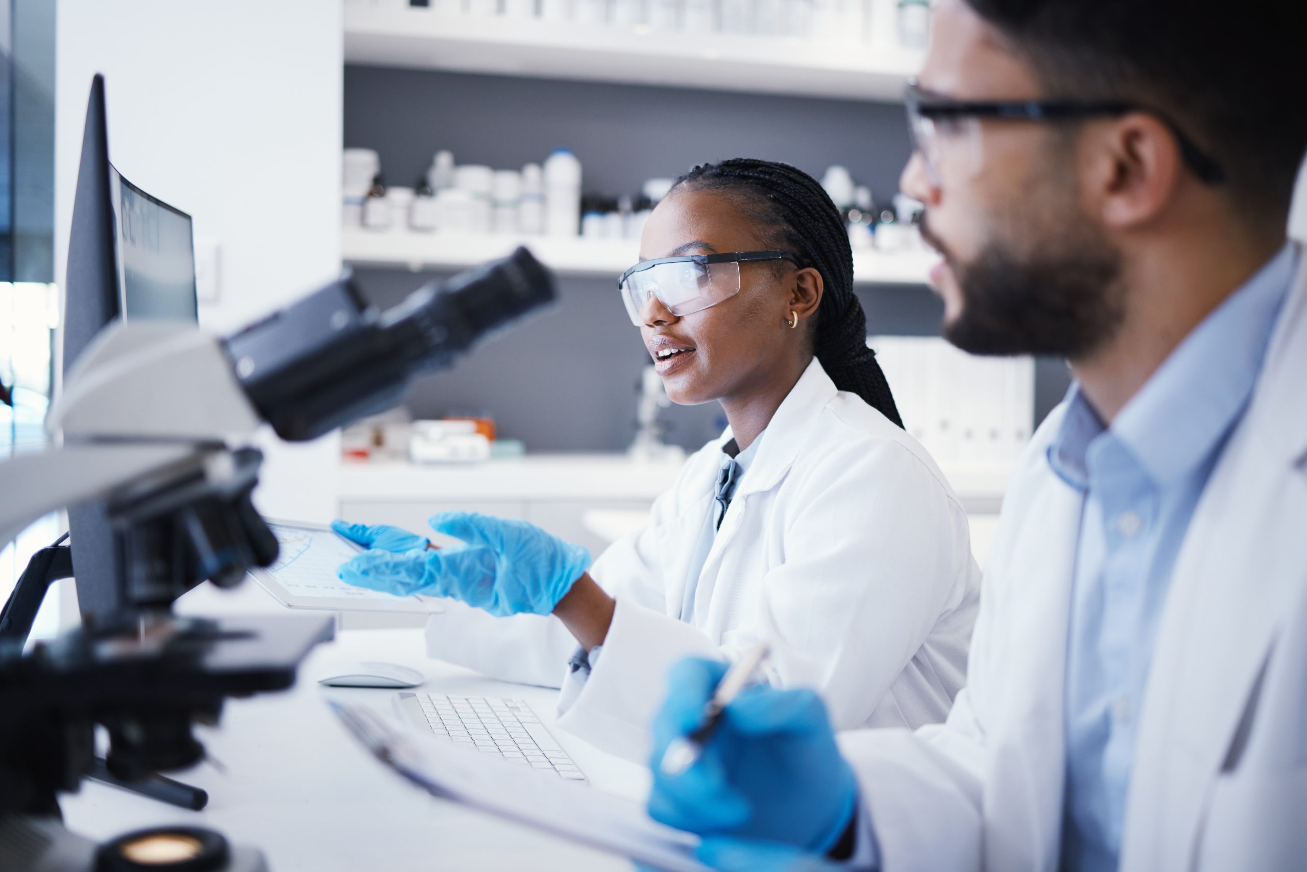 Two scientists in a lab, using a microscope and taking notes.