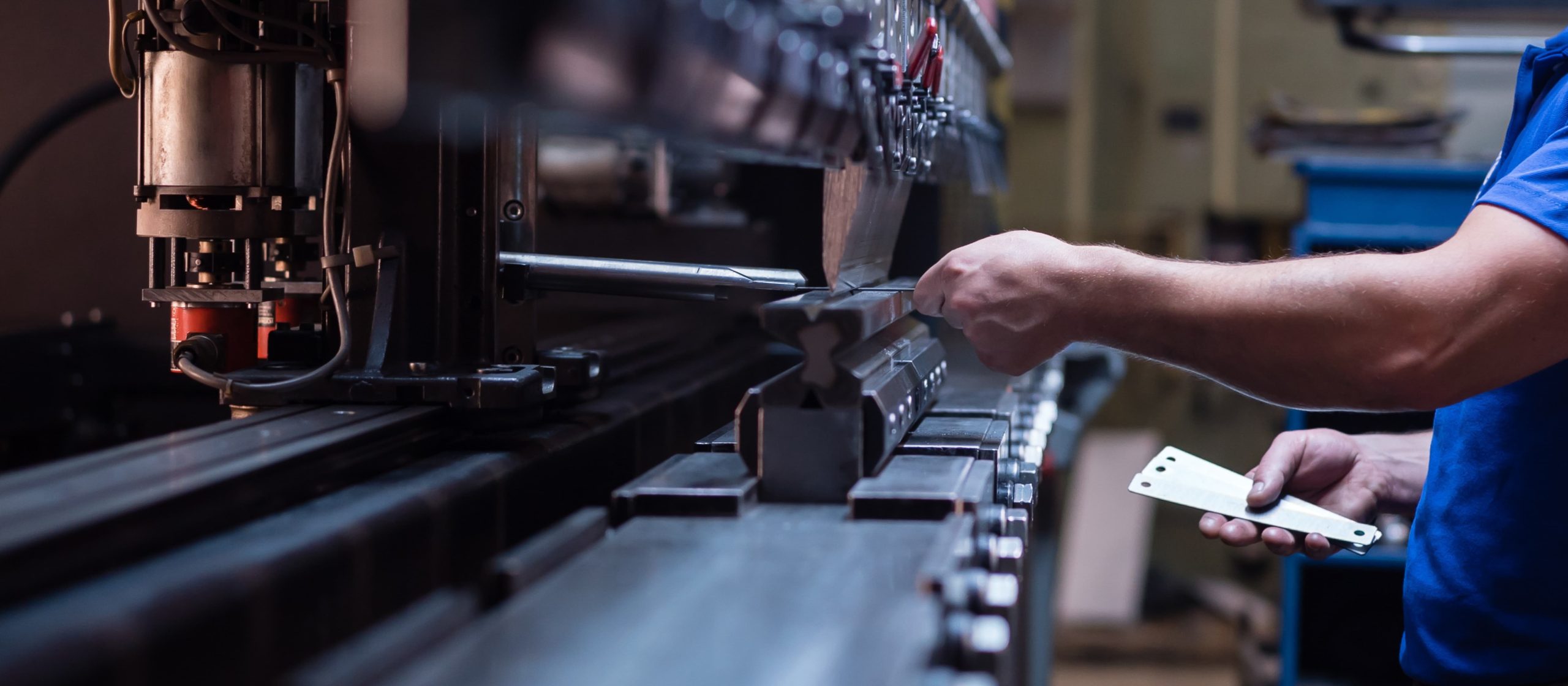 A person operating an industrial machine, holding a metal sheet in a factory setting.