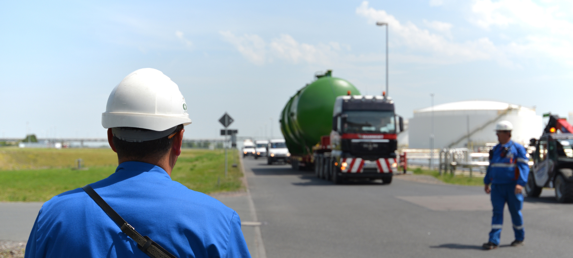 Workers in blue uniforms and hard hats at a construction site with a large green object on a truck.