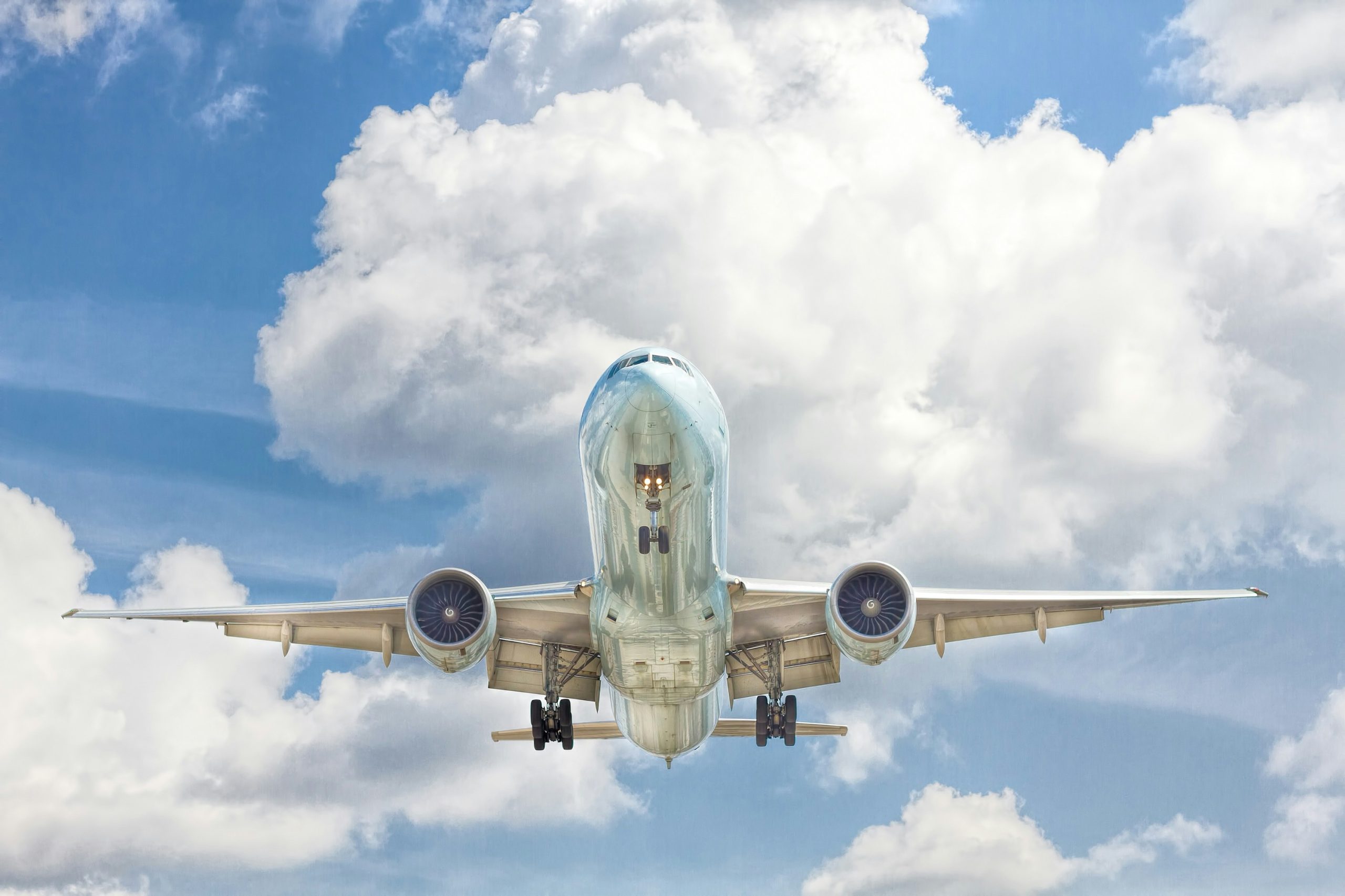 View from below of a large airplane flying against a cloudy blue sky.