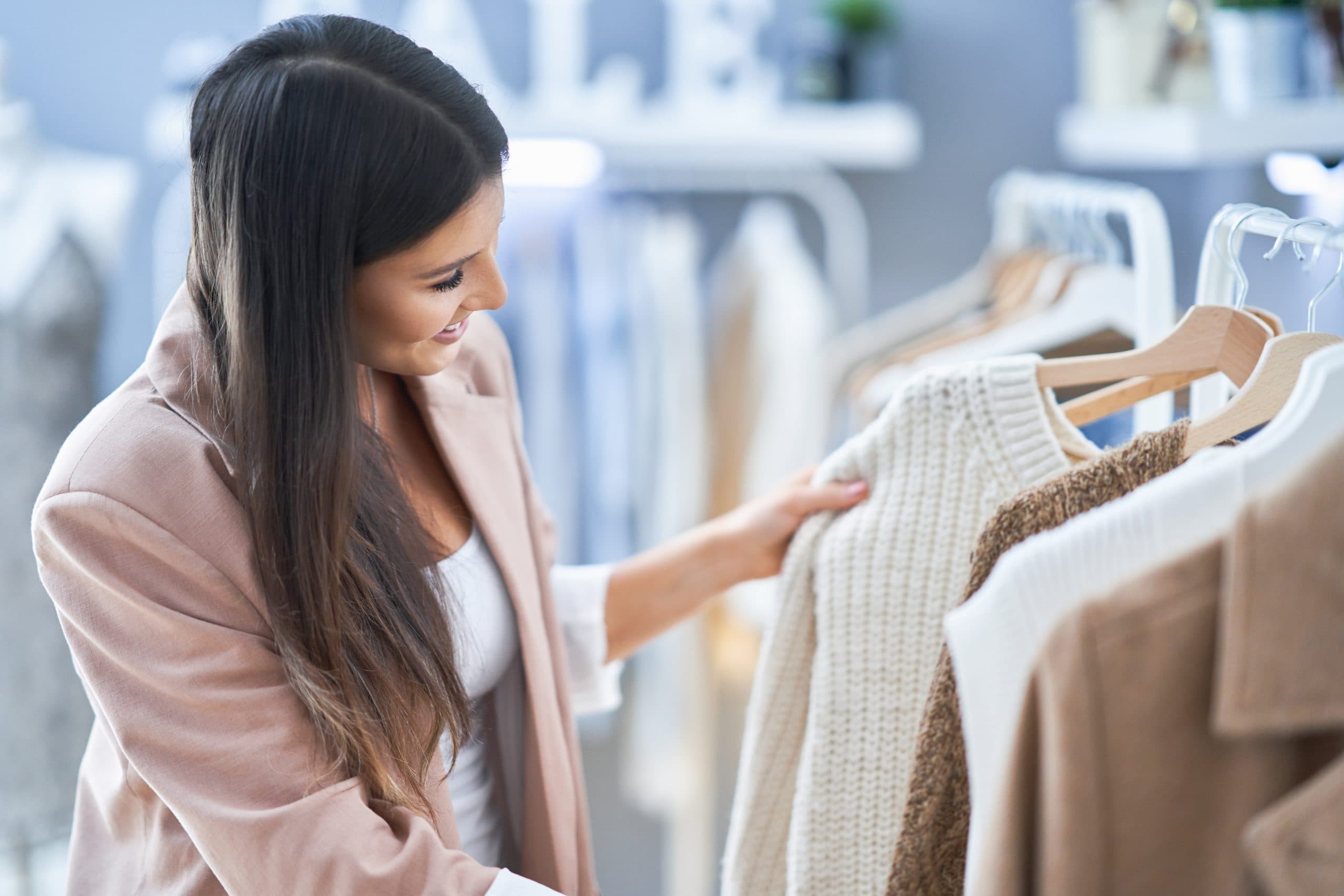 Woman shopping, examining a white knitted sweater on a clothing rack.