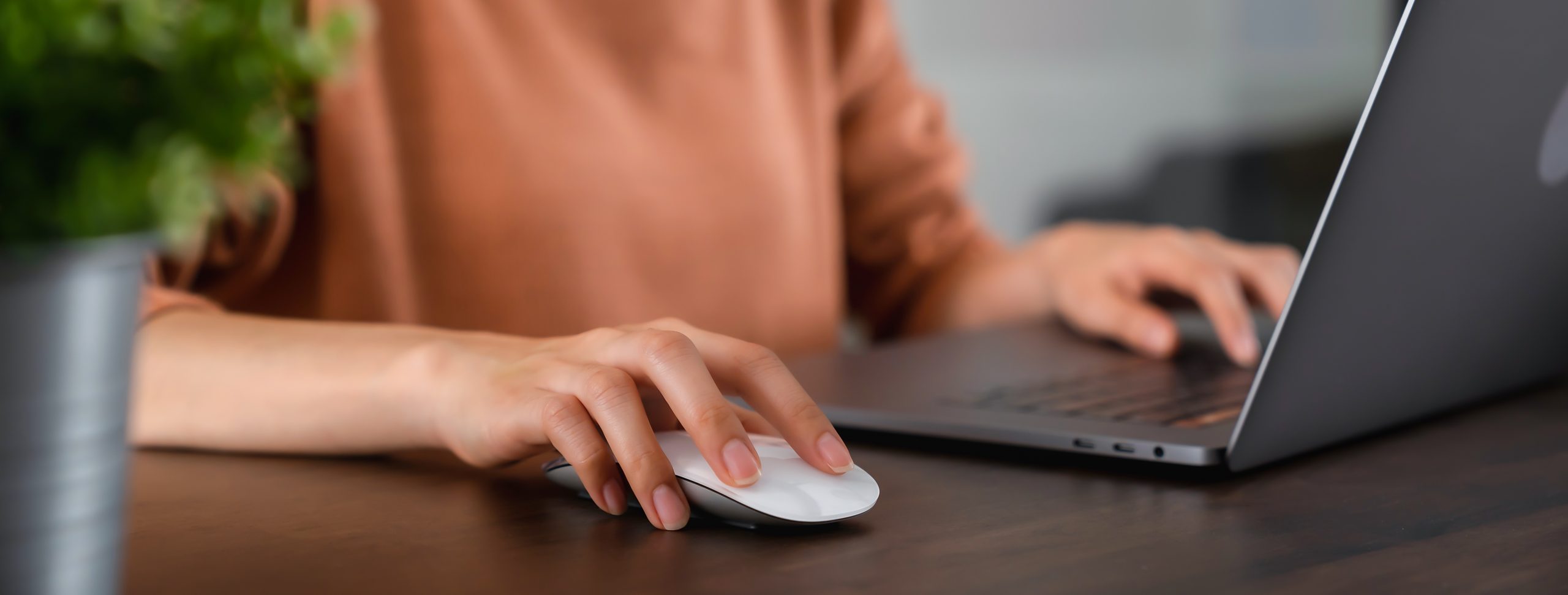 Close-up of a person using a laptop and mouse on a wooden table indoors.