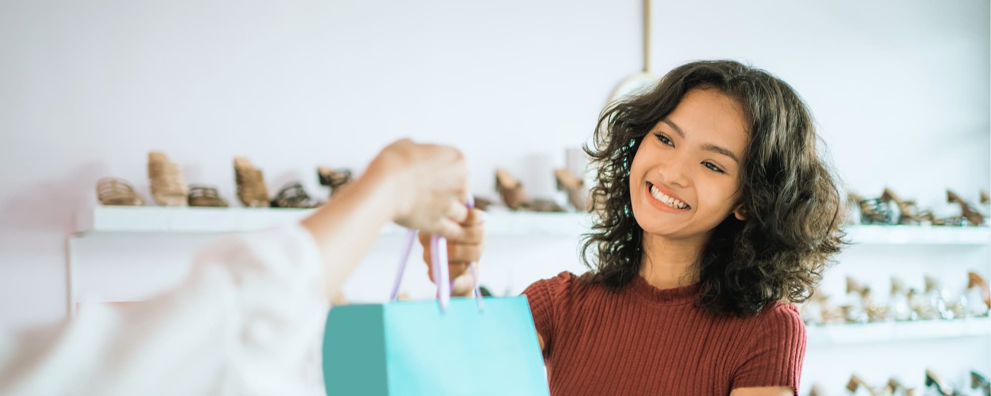 Person in a red shirt handing over a teal shopping bag in a shoe store.
