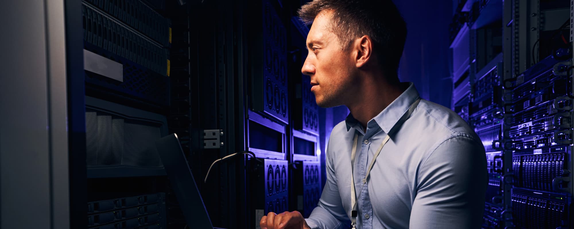 A man working in a server room with blue and purple lighting.