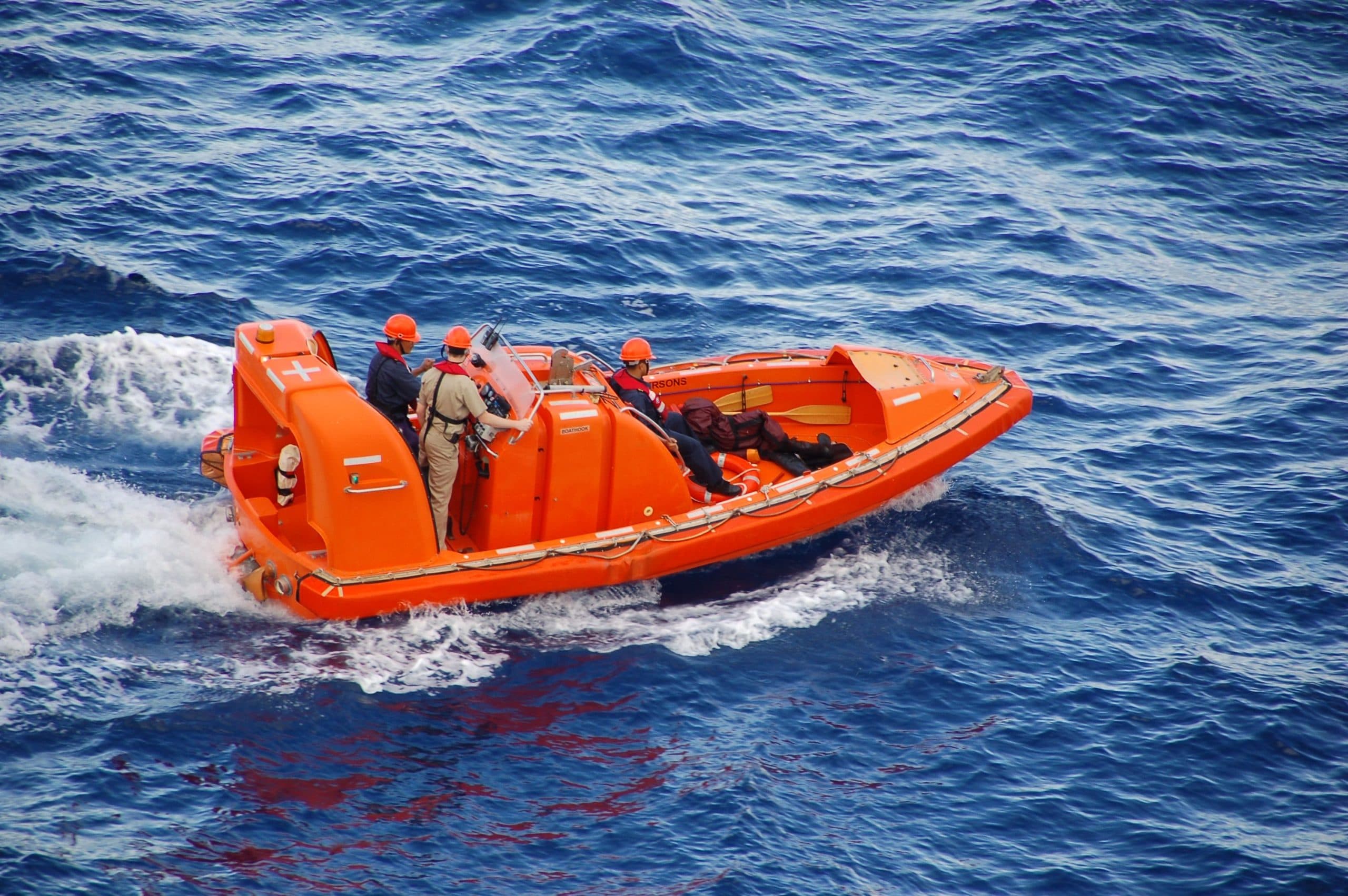 An orange lifeboat with people wearing safety helmets on a blue ocean.
