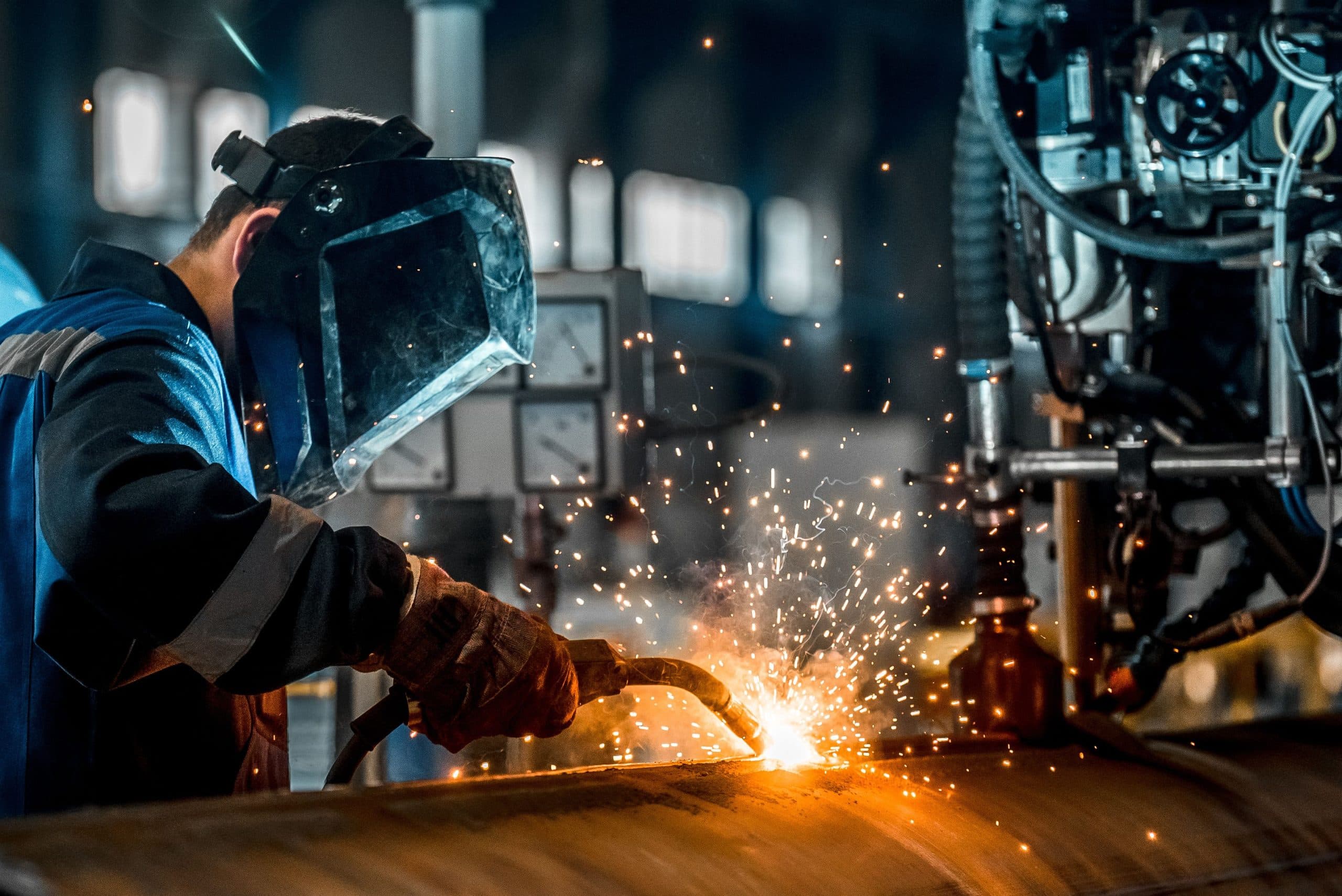 Welder in protective gear welding a metal piece with sparks flying.