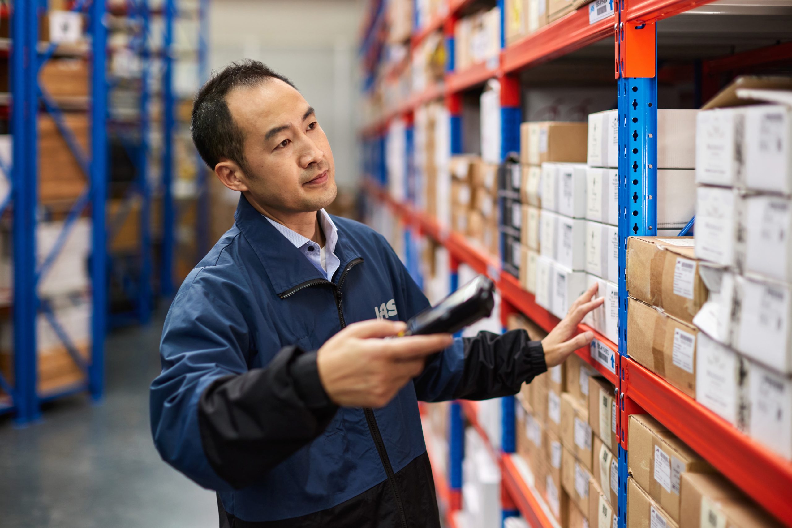 A man in a warehouse scans boxes on a shelf.