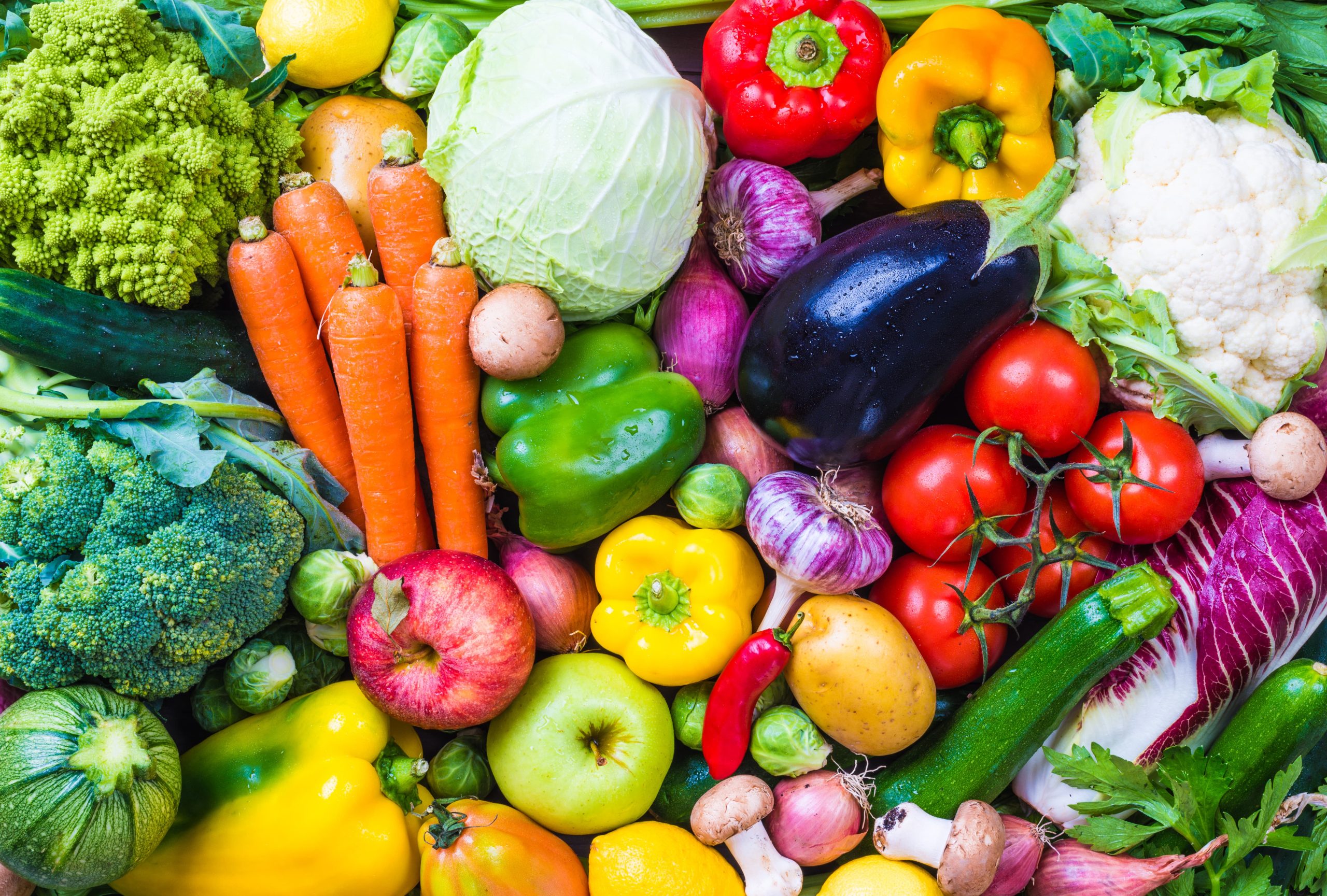 A colorful assortment of fresh vegetables and fruits including carrots, cabbage, bell peppers, eggplant, tomatoes, and more.