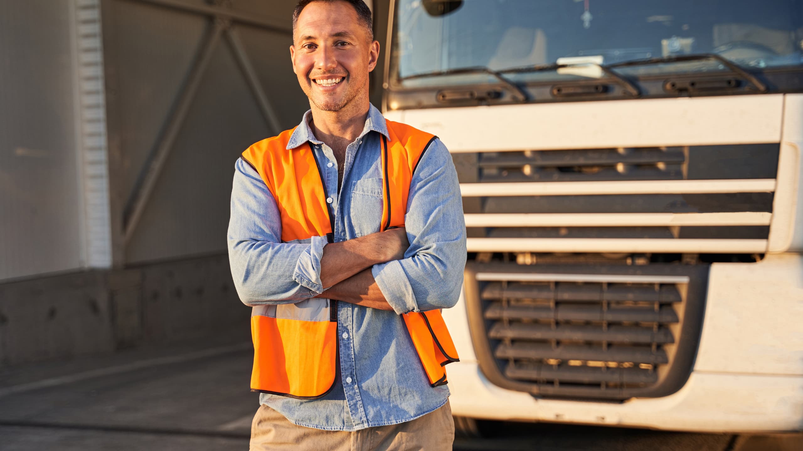 A person in an orange safety vest stands smiling in front of a truck.