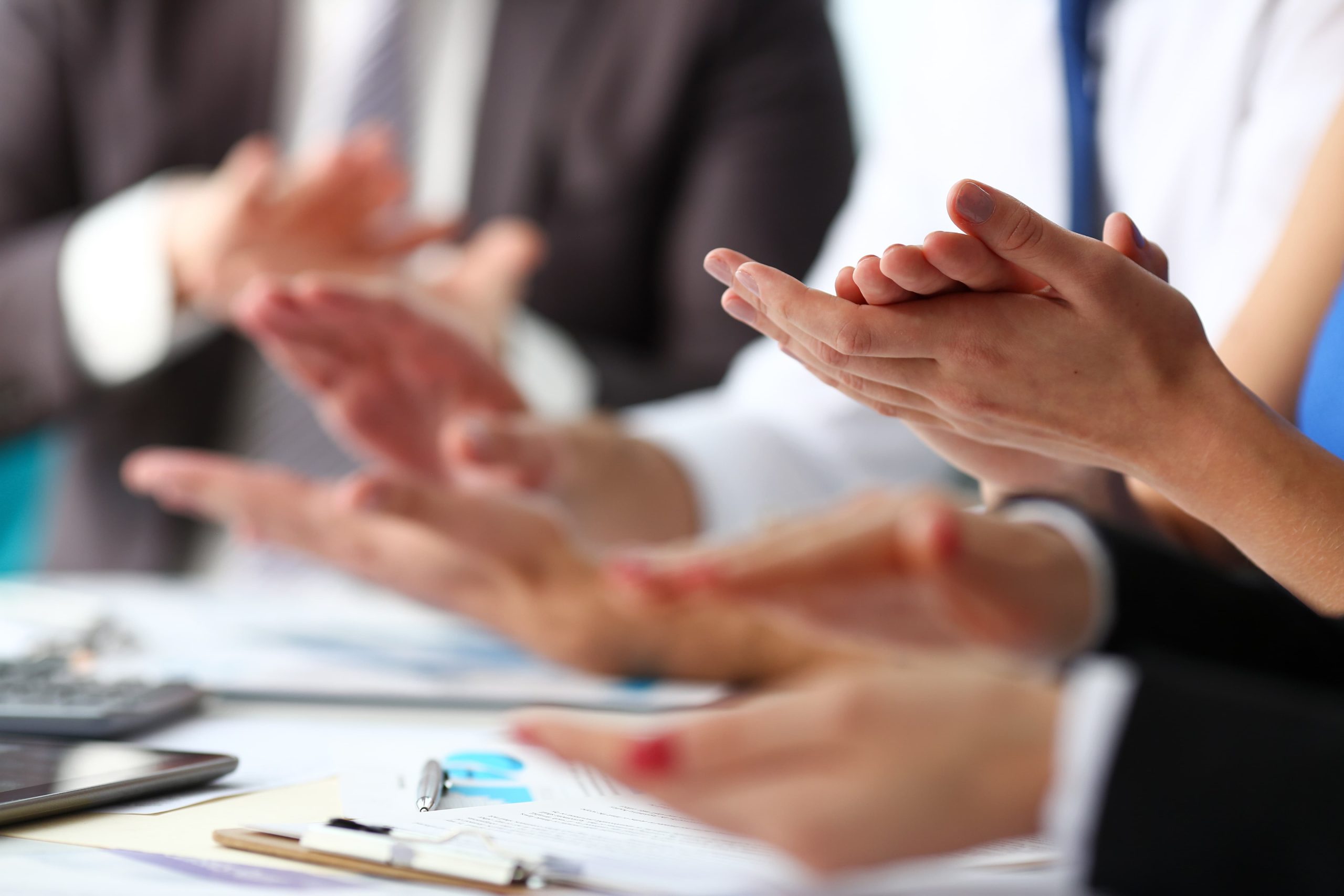 Hands clapping in a professional setting with office supplies visible on a table.