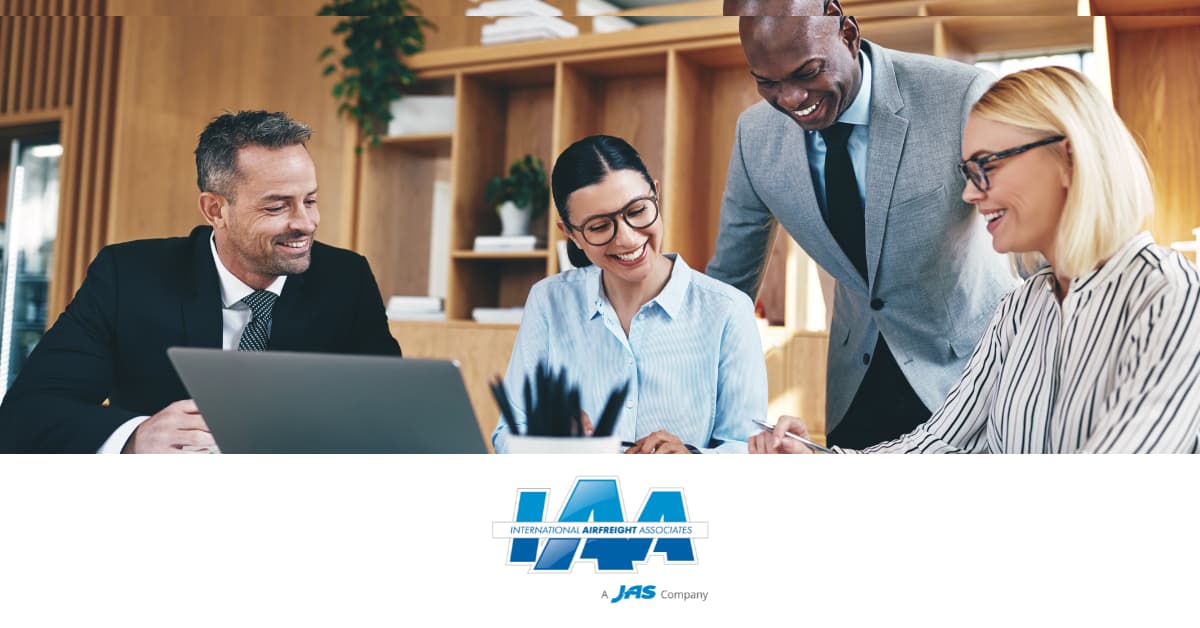 A group of four people in business attire at a meeting, smiling and collaborating.