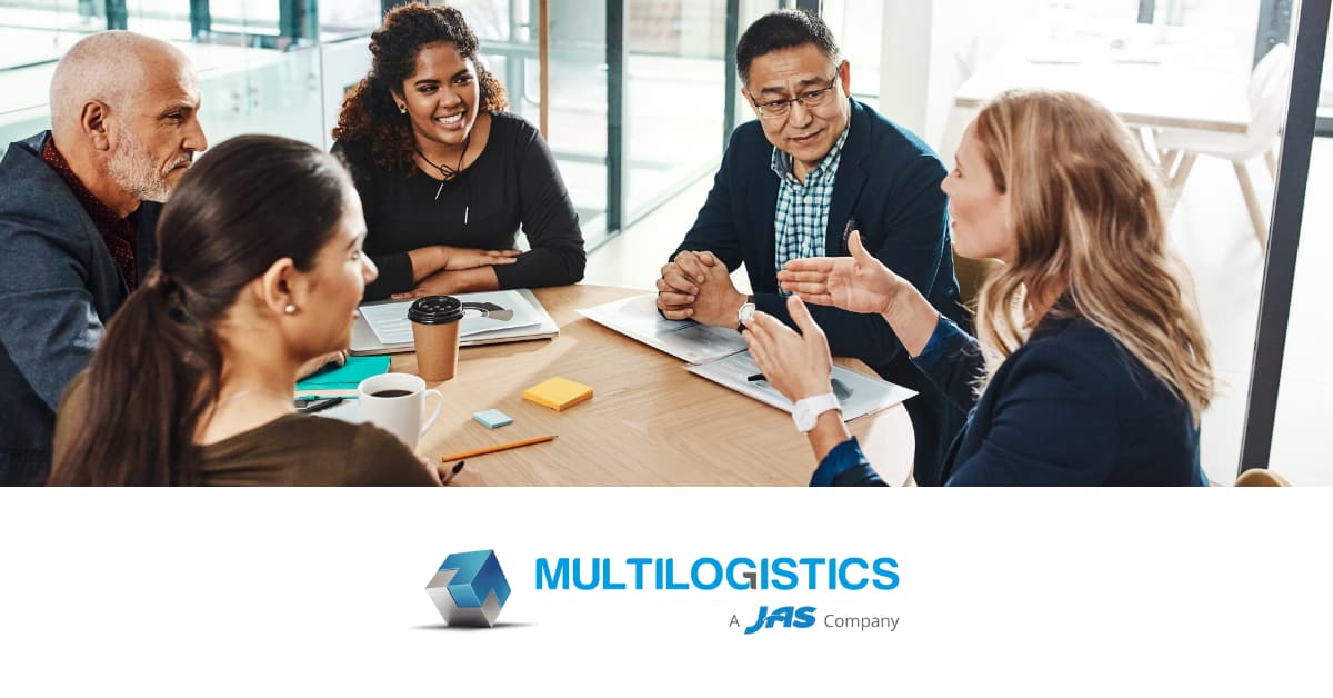 A group of five people in an office meeting around a table with notebooks and coffee cups.