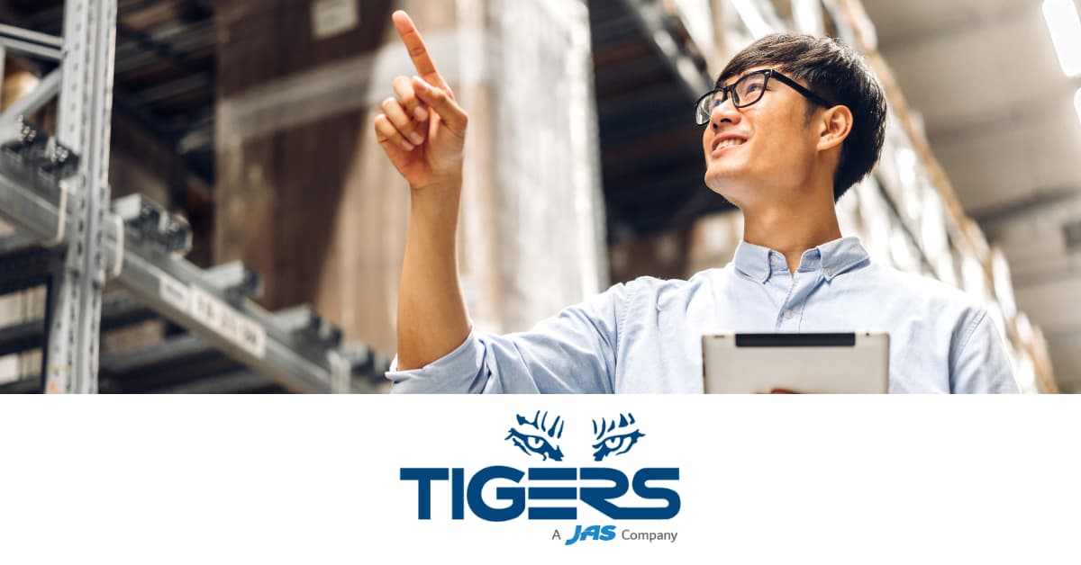 A person in a warehouse pointing upward, holding a tablet, with a TIGERS logo and text below.